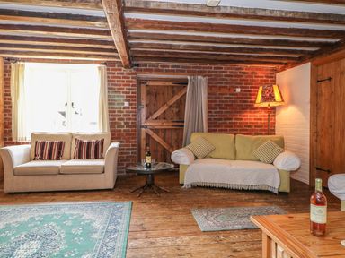 A living room with two sofas a wooden table with a bottle of wine and glasses and a floor lamp at Downs View Dairy in West Tytherley