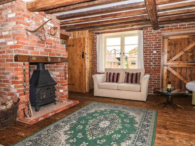 A living room with a brick fireplace wood stove beige sofa with striped cushions and wooden doors at Downs View Dairy in West Tytherley