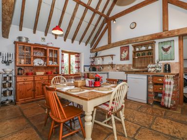 A kitchen with wooden dining table and chairs wooden cabinets and exposed ceiling beams at Downs View Dairy in West Tytherley