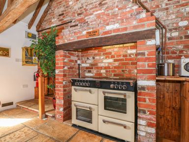 A kitchen with a large stove built into a brick fireplace and a green plant in a pot at Downs View Dairy in West Tytherley