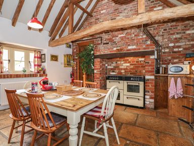 A kitchen with a wooden dining table and chairs a stove built into a brick wall and a microwave on a wooden cabinet at Downs View Dairy in West Tytherley