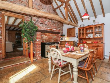 A kitchen dining area with a wooden table and chairs a brick wall with a stove and wooden cabinets at Downs View Dairy in West Tytherley