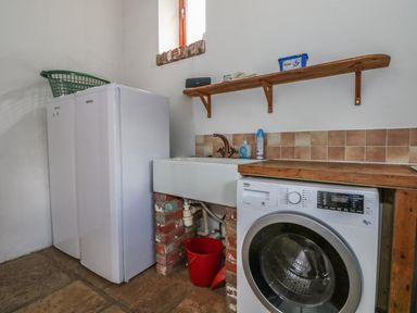 A laundry room with a washing machine sink twin freezers wooden shelf and a red bucket at Downs View Dairy in West Tytherley