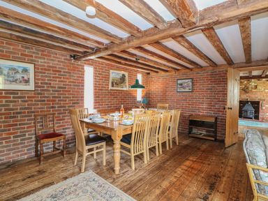 A dining room with a wooden table and chairs on wooden floor with brick walls and ceiling beams at Downs View Dairy in West Tytherley
