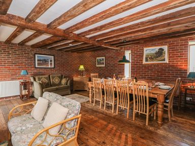 A dining room with a wooden table set with plates and chairs a patterned armchair and a green sofa under wooden ceiling beams at Downs View Dairy in West Tytherley
