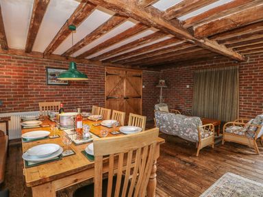 A dining area with a wooden table set with plates and glasses adjacent to a sitting area with floral cushioned chairs at Downs View Dairy in West Tytherley