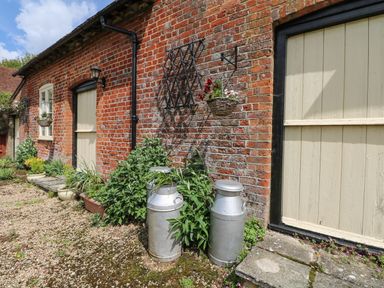 An outdoor area with two milk churns next to a brick wall with beige doors and plants at Downs View Dairy in West Tytherley