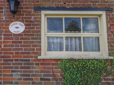 A brick wall with a window curtain ivy a lantern and a sign that reads Downs View Dairy at Downs View Dairy in West Tytherley