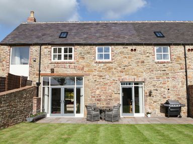 An outdoor area with a stone house, patio furniture, and a barbecue at The Turnip Barn in 