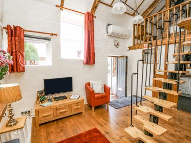 A living room with a wooden tv stand and television red armchair spiral staircase and wooden floor at Rose Cottage in Penrhiwllan