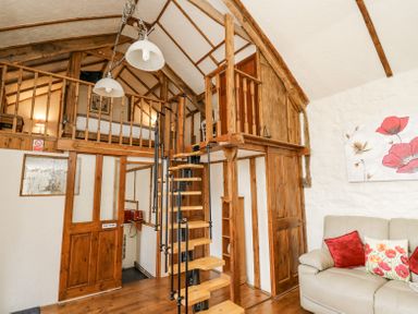 A living room with a spiral staircase leading to a loft bedroom at Rose Cottage in Penrhiwllan