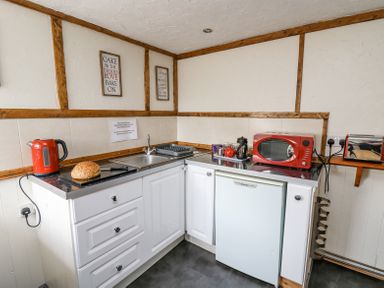 A kitchen corner with a red kettle, loaf of bread, sink, red microwave, toaster, and white cabinets at Rose Cottage in Penrhiwllan