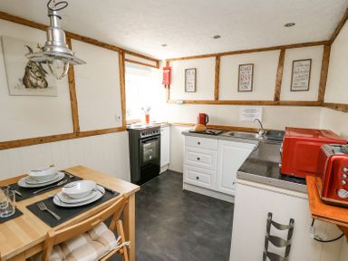 A kitchen with a dining table set for two a stove a sink a red toaster and kettle and framed signs on the wall at Rose Cottage in Penrhiwllan