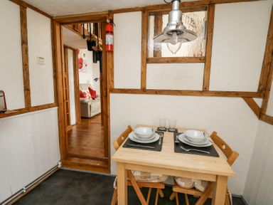 A small dining area with a wooden table set for two and a view into a living room at Rose Cottage in Penrhiwllan