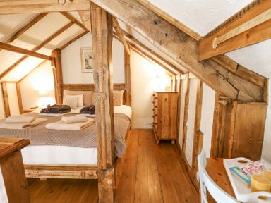 A bedroom with exposed wooden beams a bed with towels a wooden dresser and a small table with a chair at Rose Cottage in Penrhiwllan