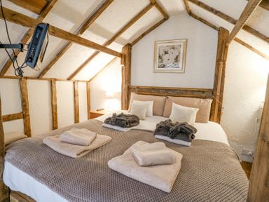 A bedroom with a double bed wooden beams a mounted television and folded towels at Rose Cottage in Penrhiwllan