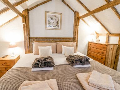 A bedroom with a bed framed by wooden beams bedside tables with lamps a chest of drawers and towels at Rose Cottage in Penrhiwllan
