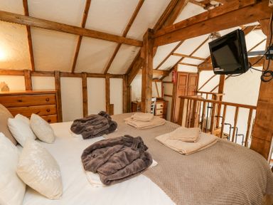 A bedroom with a bed covered with folded towels and robes a wooden dresser a desk with a chair a mounted television and wooden beams at Rose Cottage in Penrhiwllan