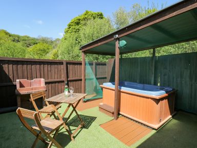 An outdoor seating area with wooden table and chairs a hot tub with a canopy and a brick barbecue at Rose Cottage in Penrhiwllan