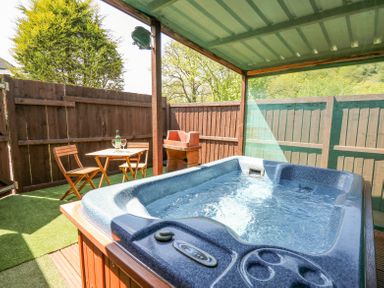 An outdoor covered patio with a hot tub wooden table and chairs and a barbecue grill at Rose Cottage Penrhiwllan