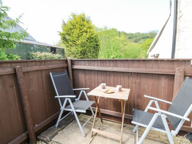 An outdoor patio with two chairs and a wooden table with mugs and a plate at Rose Cottage in Penrhiwllan
