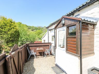 A small outdoor patio area with two chairs and a table next to a white building with a wooden porch at Rose Cottage in Penrhiwllan
