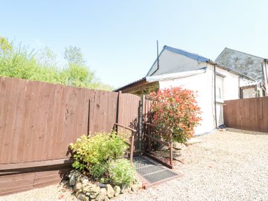 An outdoor area with a brown wooden fence brown gate plants and gravel ground near a white building at Rose Cottage in Penrhiwllan