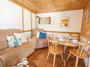 A living area with a beige sofa and armchair and a wooden dining table set with dishes and glasses at Brook Lodge in Penrhiwllan