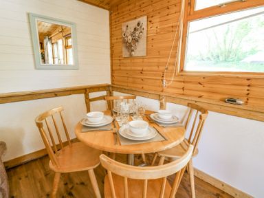 A dining area with a round wooden table set for four and wooden chairs at Brook Lodge in Penrhiwllan