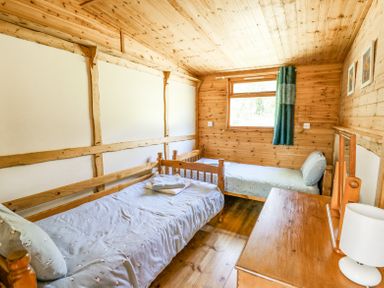 A bedroom with two single wooden beds a wooden dresser with a lamp and a window with a curtain at Brook Lodge in Penrhiwllan