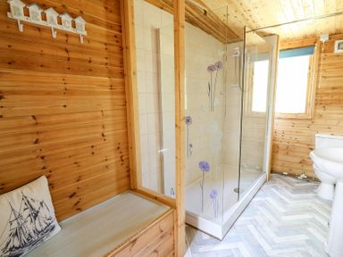 A bathroom with a wooden bench with a cushion a glass shower enclosure with floral designs a toilet and a sink at Brook Lodge in Penrhiwllan