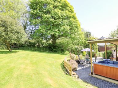 A garden with grass trees a hot tub patio furniture and a wooden fence at Brook Lodge in Penrhiwllan