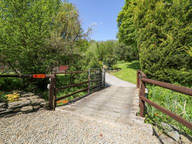 A wooden gate and small bridge over a gravel path surrounded by trees and greenery at Brook Lodge in Penrhiwllan