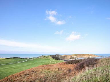 A coastal landscape with grassy hills and a building near the sea at Tan Y Goeden in Morfa Nefyn