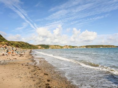 A sandy beach with waves near green hills and a blue sky at Tan Y Goeden in Morfa Nefyn