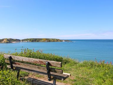 A wooden bench overlooking the sea with grassy hills and boats in the water at Tan Y Goeden in Morfa Nefyn