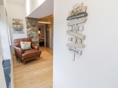 An armchair with a floral cushion next to a stone wall in a room with wooden floor and decorative signs on white walls at Pentowyn in Holyhead