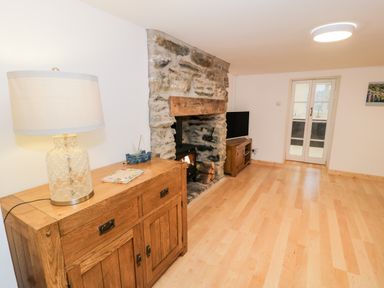 A living room with a wooden cabinet and lamp a stone fireplace and a television on a stand at Pentowyn in Holyhead
