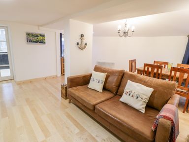 A living room with a brown leather sofa and wooden dining table with chairs at Pentowyn in Holyhead