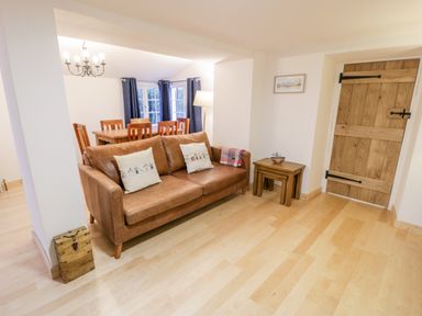 A living room with a brown leather sofa and dining table with chairs near windows at Pentowyn in Holyhead
