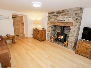 A living room with a stone fireplace wooden furniture and a wood burning stove at Pentowyn in Holyhead