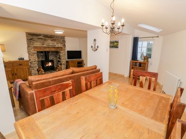 A living and dining room with wooden table and chairs a leather sofa stone fireplace and a television at Pentowyn in Holyhead