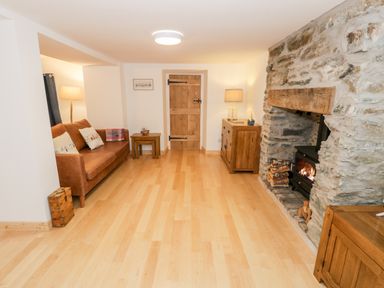 A living room with a brown sofa wooden furniture and a stone fireplace with fire at Pentowyn in Holyhead