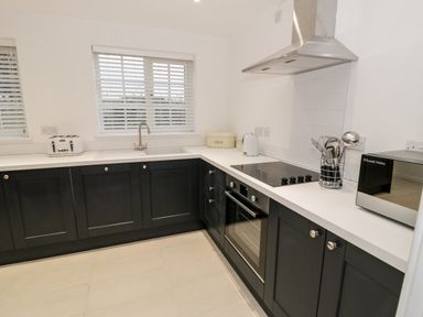 A kitchen with black lower cabinets white countertops a built-in oven stovetop microwave toaster and a window with blinds at Pentowyn in Holyhead