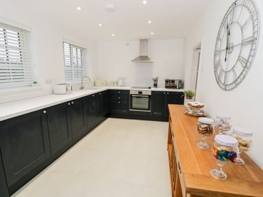 A kitchen with black cabinets white countertops appliances and a wooden sideboard with jars of sweets and cookies at Pentowyn in Holyhead