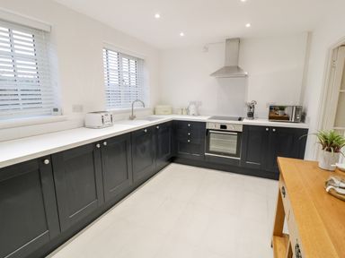 A kitchen with dark cabinets white countertops a stove oven toaster microwave and a wooden table at Pentowyn Holyhead