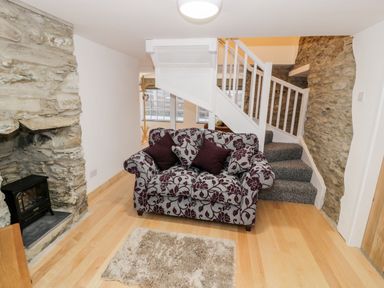 A living room with a patterned sofa near stone walls and a staircase at Pentowyn in Holyhead