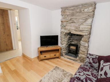 A corner of a living room with a stone fireplace electric stove television on a wooden stand and patterned sofa at Pentowyn in Holyhead
