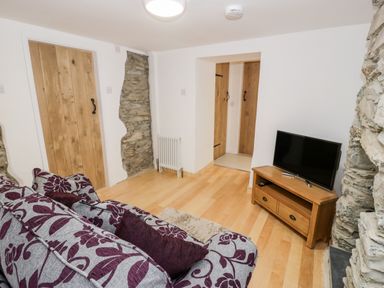 A sitting room with a floral patterned sofa a wooden TV stand with a flat screen TV wooden doors exposed stone walls and light wood flooring at Pentowyn in Holyhead