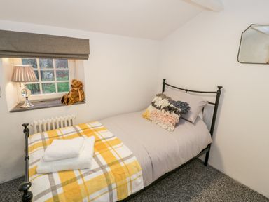 A small bedroom with a single bed a yellow plaid blanket towels on the bed a lamp and teddy bear on the window sill at Pentowyn in Holyhead